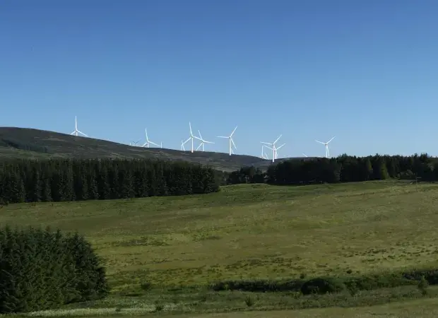 Une dizaine d'éoliennes au loin sur une colline verdoyante.